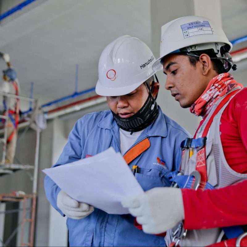 Two construction workers engaged in a safety discussion on a construction site with one worker holding a document